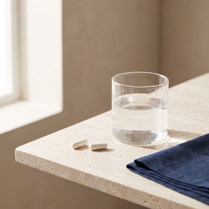 Zwei Kapseln neben einem Glas Wasser auf hellem Stein